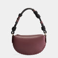 Luxury mini shoulder bag in burgundy, handcrafted in collaboration with AVDW Antwerp from vegan, sustainable, and cruelty-free Kayla Fabric™—an eco-friendly leather alternative. Designed by a Dutch designer, this authentic bag features a compact, curved design with hand-knotted cords and soft gold accents, blending artistry with practicality. The best designer handbag for those seeking ethical elegance. Made in Europe.