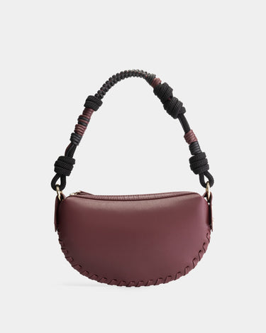 Luxury mini shoulder bag in burgundy, handcrafted in collaboration with AVDW Antwerp from vegan, sustainable, and cruelty-free Kayla Fabric™—an eco-friendly leather alternative. Designed by a Dutch designer, this authentic bag features a compact, curved design with hand-knotted cords and soft gold accents, blending artistry with practicality. The best designer handbag for those seeking ethical elegance. Made in Europe.