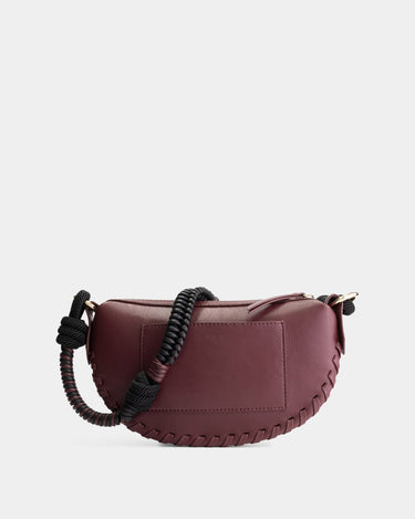 Luxury mini shoulder bag in burgundy, handcrafted in collaboration with AVDW Antwerp from vegan, sustainable, and cruelty-free Kayla Fabric™—an eco-friendly leather alternative. Designed by a Dutch designer, this authentic bag features a compact, curved design with hand-knotted cords and soft gold accents, blending artistry with practicality. The best designer handbag for those seeking ethical elegance. Made in Europe.