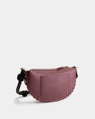 Luxury mini shoulder bag in burgundy, handcrafted in collaboration with AVDW Antwerp from vegan, sustainable, and cruelty-free Kayla Fabric™—an eco-friendly leather alternative. Designed by a Dutch designer, this authentic bag features a compact, curved design with hand-knotted cords and soft gold accents, blending artistry with practicality. The best designer handbag for those seeking ethical elegance. Made in Europe.