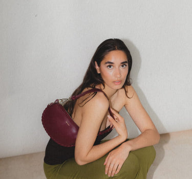 Brunette model wearing Racoon Mini in Lily Maroon over the shoulder wearing a green skirt and black top