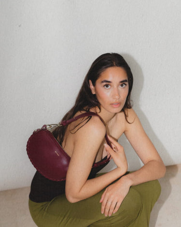 Brunette model wearing Racoon Mini in Lily Maroon over the shoulder wearing a green skirt and black top