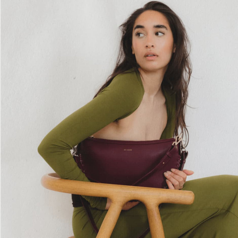 Brunette Model sitting and holding Racoon Lily Maroon shoulder bag wearing olive green outfit