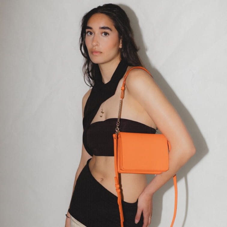 Firefly Parrot Orange cross-body bag with gold chain and gold Iris Maree logo worn by brunette model, made environmentally conscious material Kayla Fabric