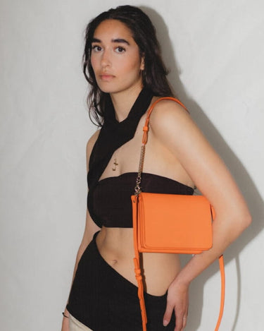 Firefly Parrot Orange cross-body bag with gold chain and gold Iris Maree logo worn by brunette model, made environmentally conscious material Kayla Fabric